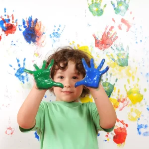 Smiling child holding up paint-covered hands during creative play