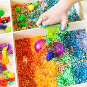 Child exploring a colourful sensory tray with scoops and coloured rice