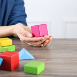 ABA therapist with colorful building blocks at wooden table, closeup